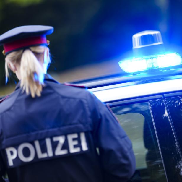 Eine Polizistin steht neben einem Einsatzfahrzeug mit eingeschaltetem Blaulicht.